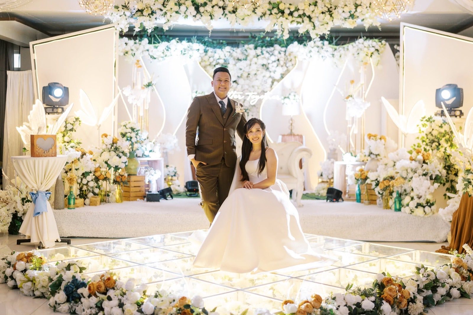 A real bride and groom at their Casa de Corazon reception stage, white floral backdrop